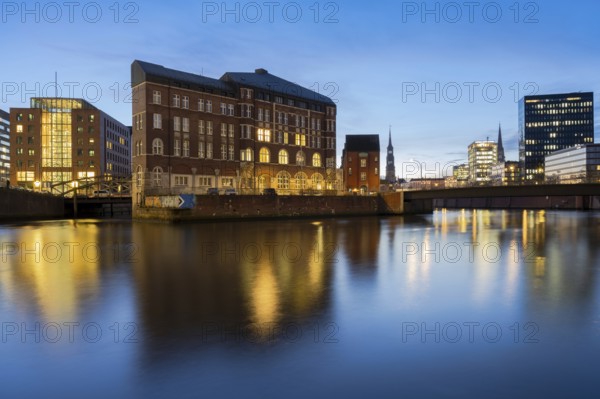 View from Oberbaum Bridge of the Zollkanal and Teerhof at blue hour with reflections in the water and light cloudiness in the background, Speicherstadt, Hamburg, Germany