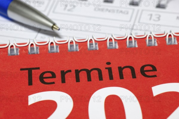 Close-up of red spiral calendar with blue pen, appointment calendar