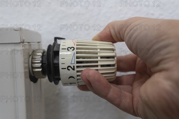 A hand grabs the thermostat head of a radiator to adjust the temperature. This image symbolizes control over the indoor climate and comfort in a modern home. The scene conveys a sense of functionality and homely comfort