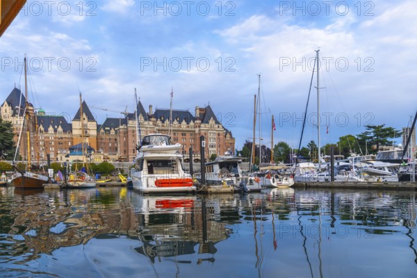 Luxury yachts and sailboats are moored in front of the fairmont empress hotel, reflecting in the calm water of victoria harbor on a sunny summer day on vancouver island, british columbia