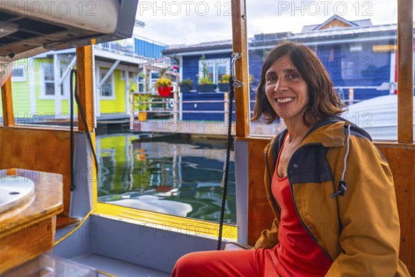Happy tourist smiling while enjoying a sunny summer day on a small boat trip visiting the colorful floating houses community of fisherman's wharf park in victoria, british columbia
