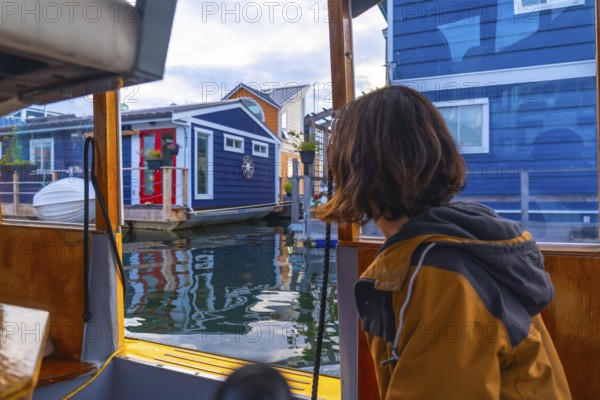 Tourist enjoying a boat tour passing by the colorful floating houses of fisherman's wharf park in victoria, british columbia, on a summer day with reflections on the water