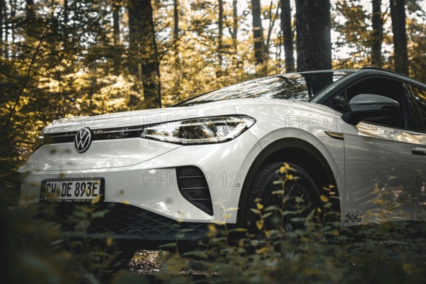 A white car is parked in an autumn-lit forest, VW ID4 electric car, Deer Carsharing, Calw, Germany