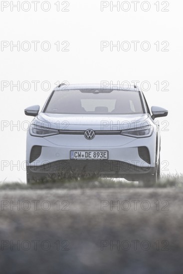 A white car seen from the front in a morning haze in an open landscape, VW ID4 electric car, Deer Carsharing, Calw, Germany