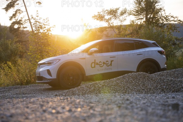 White car on gravel under the evening sun, surrounded by nature, quiet atmosphere, VW ID4 electric car, deer car sharing, Calw, Germany