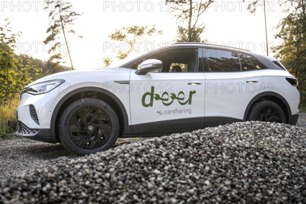 A white car stands on gravel against a forest backdrop at sunset, VW ID4 electric car, deer car sharing, Calw, Germany