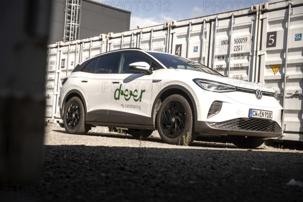 White car parked next to large grey containers under a blue sky in an urban environment, VW ID4 electric car, Deer Carsharing, Calw, Germany