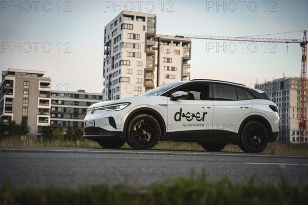 A white car is parked on a street with modern buildings in the background, VW ID4 electric car, Deer Carsharing, Calw, Germany