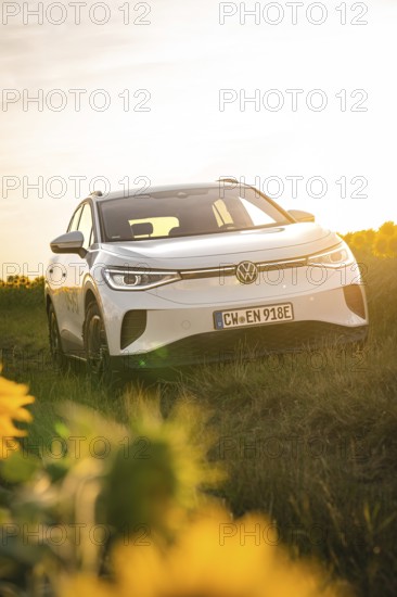 A white car in a meadow next to sunflowers at sunset, VW ID4 electric car, Deer Carsharing, Calw, Germany