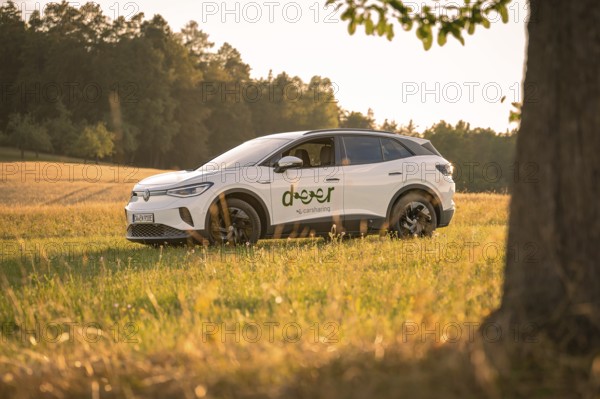 A white car in a meadow at sunset against a wooded background, VW ID4 electric car, deer car sharing, Calw, Germany