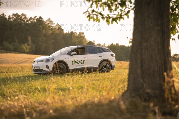 White car at sunset in a field, a tree in the foreground, rural atmosphere, VW ID4 electric car, deer car sharing, Calw, Germany