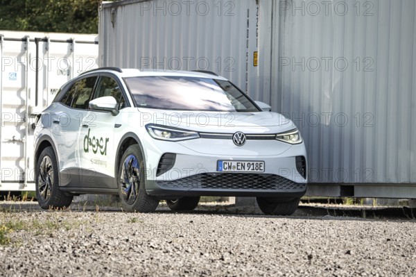 White car parked in a rocky place next to large metal containers, modern ambiance, VW ID4 electric car, deer car sharing, Calw, Germany