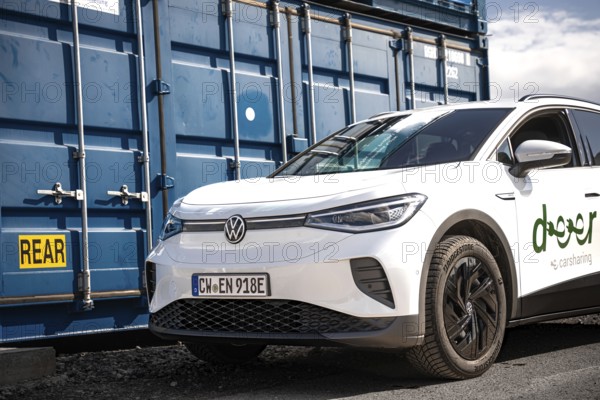 White car in an urban location next to a blue container, industrial atmosphere, VW ID4 electric car, deer car sharing, Calw, Germany