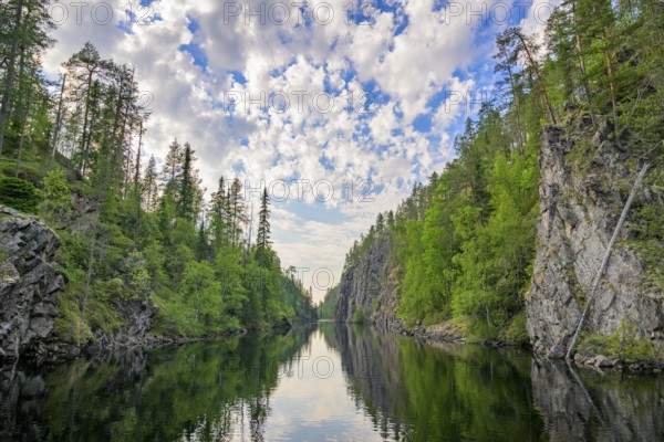 A calm lake lies in a wooded gorge, surrounded by tall rocks and reflecting the sky covered with clouds Julma-Ölkky Canyon Gorge, Hossa National Park, Irni, Northern Ostrobothnia, Finland