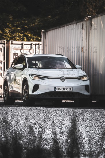 A car on a gravel field next to stacked containers in the shade, VW ID4 electric car, Deer Carsharing, Calw, Germany