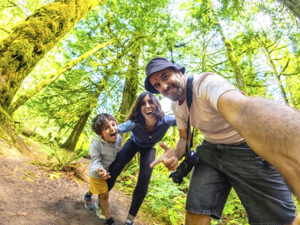 Happy family taking a selfie in the beautiful cathedral grove forest on vancouver island, british columbia, canada, enjoying a summer day surrounded by giant trees and lush greenery