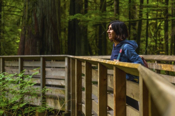 Woman enjoys a summer walk through the serene cathedral grove on vancouver island, canada. The lush greenery and towering trees create a peaceful atmosphere along the wooden path