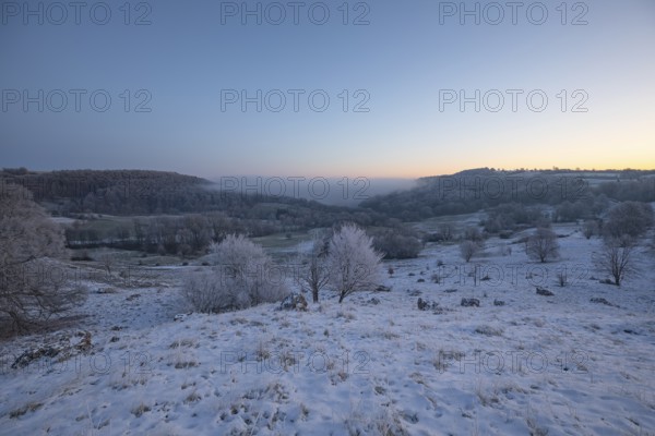 An impressive winter landscape on Randecker Maar near Ochsenwang, where a mystical sea of fog covers the surrounding area. The freezing cold of the morning is reinforced by the snow-covered hills and the soft light. This scene conveys a peaceful, enchanted atmosphere and shows the quiet beauty of nature in winter