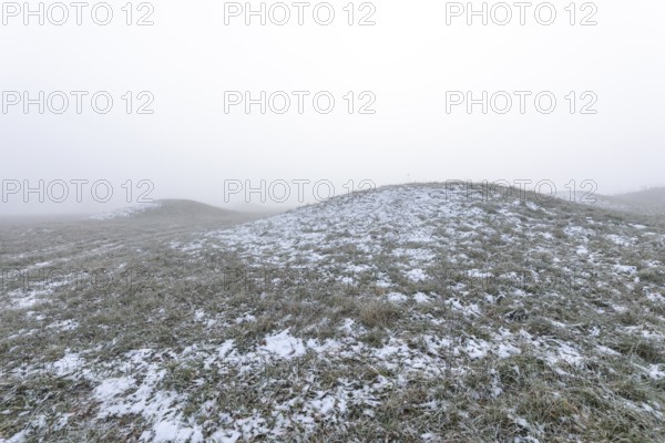 Mystical Celtic burial mounds in winter fog near Erkenbrechtsweiler. Snowy historic burial sites on Heidengraben in the Swabian Jura in an atmospheric winter atmosphere