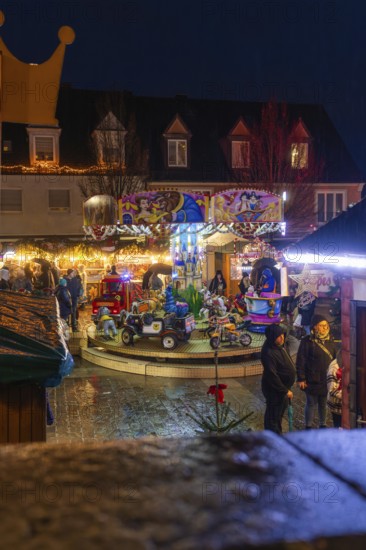 Illuminated carousel with people on a Christmas playground at night, Böblingen Christmas market, Germany