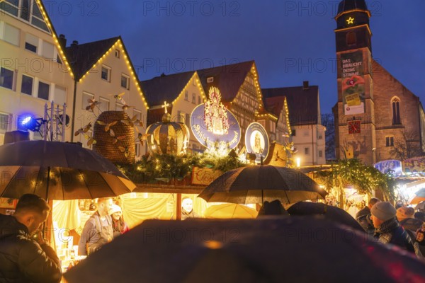 Crowd of people with umbrellas at an illuminated Christmas market in front of a church at night, Böblingen Christmas market, Germany