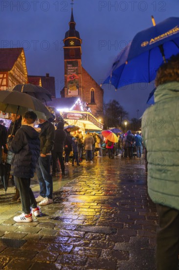 People with umbrellas on a wet Christmas market at night with illuminated church in the background, Böblingen Christmas market, Germany