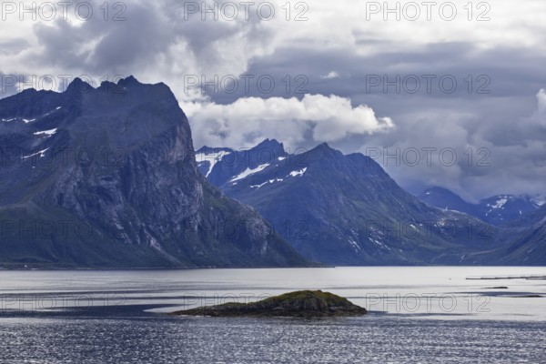 Unique view of rugged mountains and a small island in a quiet fjord under a cloudy sky, Norway
