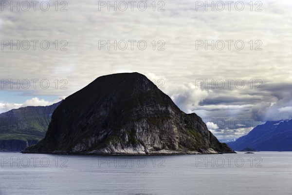 Barren rocky island surrounded by calm sea and cloudy sky, Norway