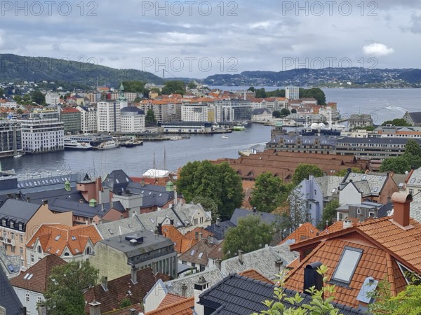 View of the city of Bergen with red roofs, a harbor and surrounding mountains under cloudy sky, Bergen Norway