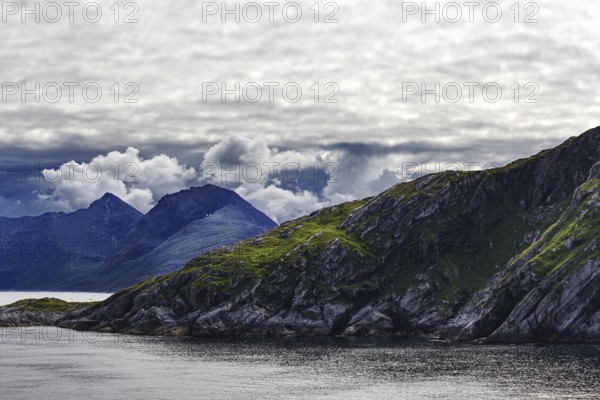 Ocean rocks with dramatic clouds and mountains, Norway