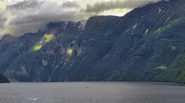 Dramatic fjord under low-hanging clouds surrounded by steep, green mountains, Norway