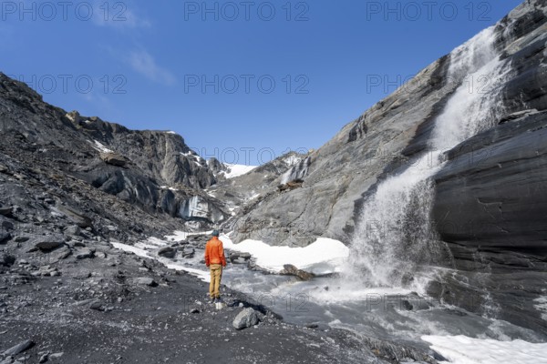 Tourist standing at a glacier stream, glacier ice and waterfall, Worthington Glacier State Recreational Site, Chugach Mountains, Alaska, USA