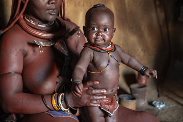 Himba woman sitting with baby in traditional hut, Himba village, Kaokoveld, Kunene, Namibia