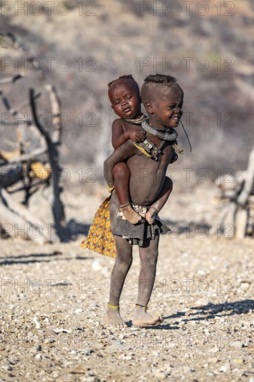Himba child carrying baby piggyback, traditional Himba village, Kaokoveld, Kunene, Namibia