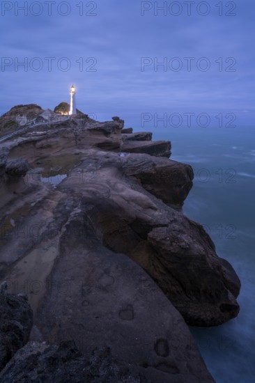 Castlepoint lighthouse on a rock, ocean, evening, blue hour, illuminated, long exposure. Castlepoint, Wairarapa Coast, Wellington Region, North Island, New Zealand