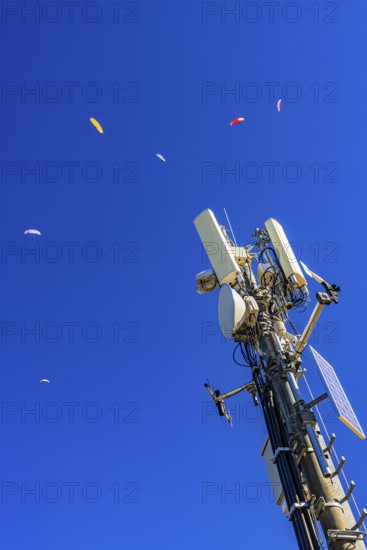 Paragliders with colored paragliders fly over the transmitter and cell phone tower at the summit of Corne de Sorebois, Val d'Anniviers, Valais Alps, Canton of Valais, Switzerland