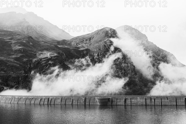 Fog rises over the dam of the Lac de Moiry reservoir, black and white photo, Val d'Anniviers, Valais Alps, Canton of Valais, Switzerland