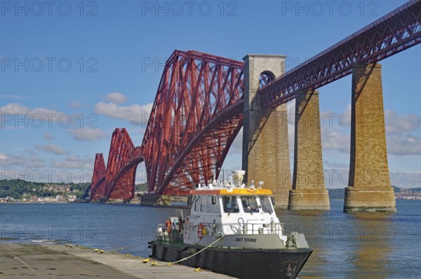 A boat next to a big red bridge against a blue sky in water, tourism, railway bridge, Firth of Forth, Edinburgh, Scotland, United Kingdom