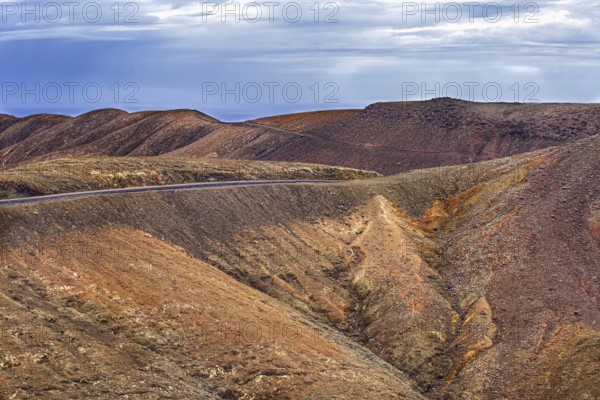 Barren volcanic landscape with a road under cloudy sky, Pajara Fuerteventura, Canary Island