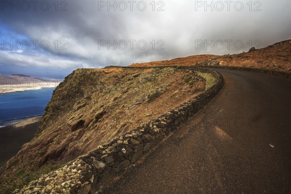 Coastal road along a dramatic cliff under a cloudy sky, Haria Lanzarote, Canary Island