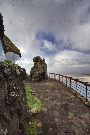 Rocky path with railing at Mirador del Rio viewpoint in cloudy sky, Haria Lanzarote, Canary Island