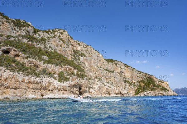 Picturesque rocky coast, motor boat off cliffs and blue sea, Golfo di Orosei, Baunei, Sardinia, Italy