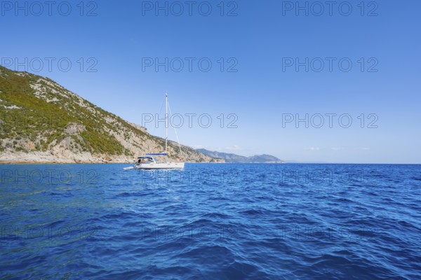 Sailing boat anchors off picturesque rocky coast, cliffs and blue sea, Golfo di Orosei, Baunei, Sardinia, Italy