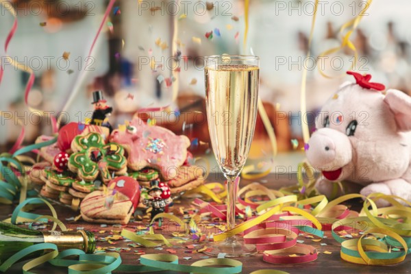 Falling confetti over champagne glass surrounded by New Year cookies, streamers and plush pig