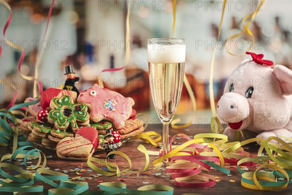 Filled champagne glass surrounded by New Year cookies, streamers and plush pig