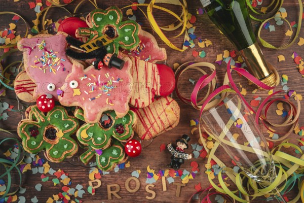 New Year cookies, confetti and prosit lettering next to champagne bottle