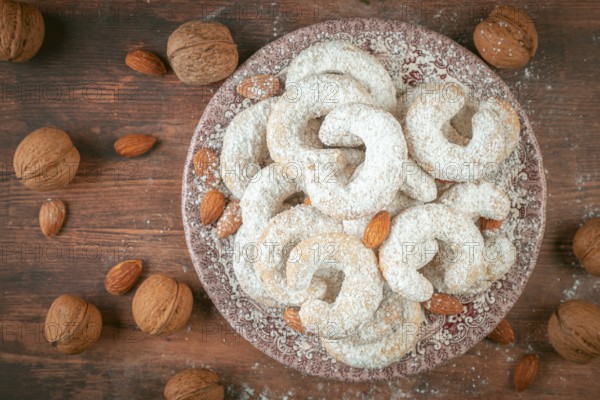 Vanilla croissants on a plate surrounded by walnuts and almonds