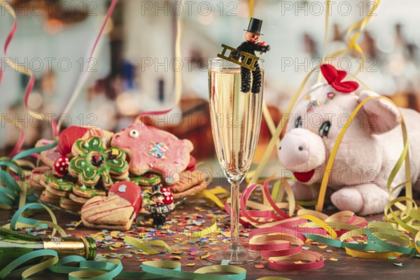 Festive champagne glass surrounded by New Year cookies, streamers and plush pig