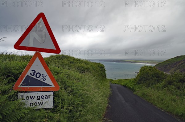 A steep road sign stands out against a dramatic coastal landscape, Cornwall, United Kingdom