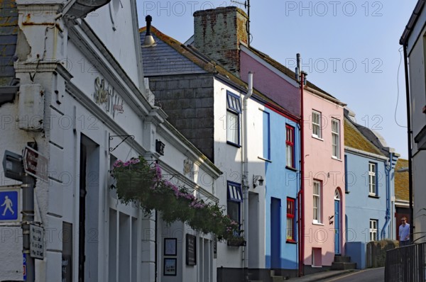 Colourful houses line a narrow village street under clear skies, Cornwall, United Kingdom